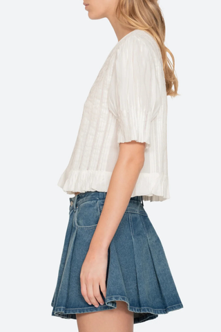 side profile model wearing Alberte Top white cotton V-neckline
Short sleeves
Delicate pintuck pleats
Subtle peplum hem
button front