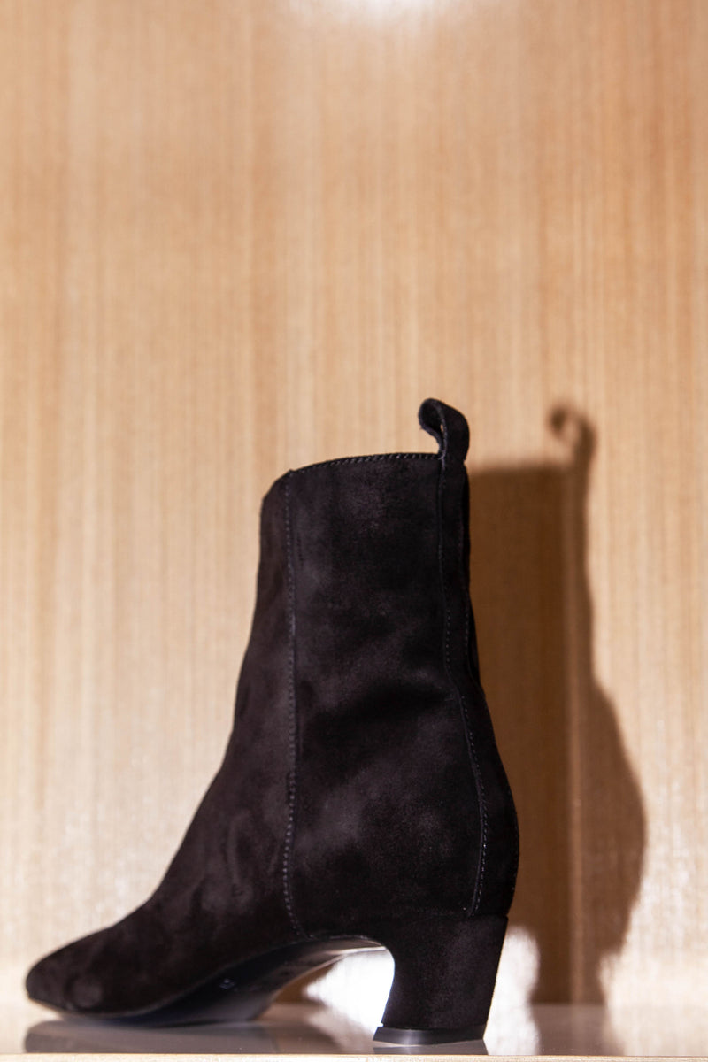 black suede boots from a back angle with curved heel and yellow tinted wood background