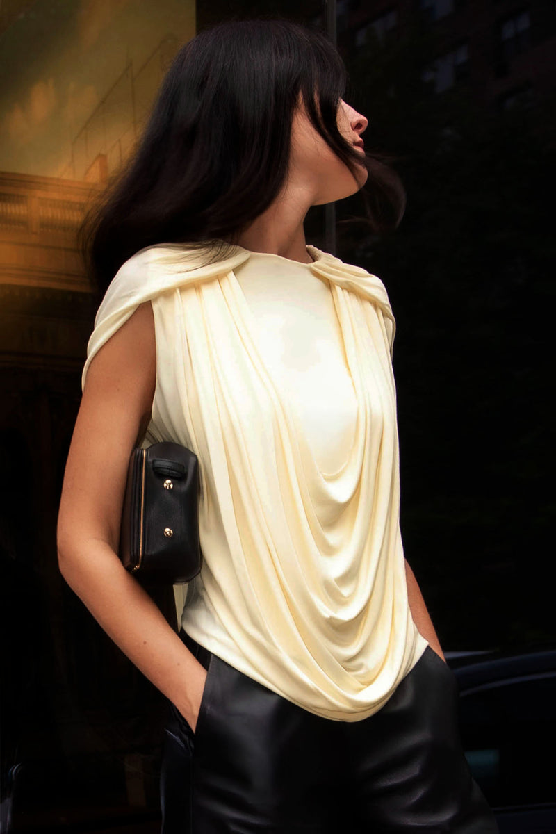 Model wearing yellow draping top and black leather pants and a black leather bag with black with sections of gold background