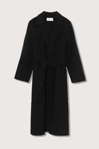 flat lay Carlita Coat Black wool Single breasted long coat. Three covered buttons. Slightly oversized. Tailored collar. Raglan sleeves. Patch pockets on front. Single vent at center back. Self fabric belt.