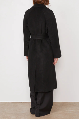 back profile model wearing Carlita Coat Black wool Single breasted long coat. Three covered buttons. Slightly oversized. Tailored collar. Raglan sleeves. Patch pockets on front. Single vent at center back. Self fabric belt.