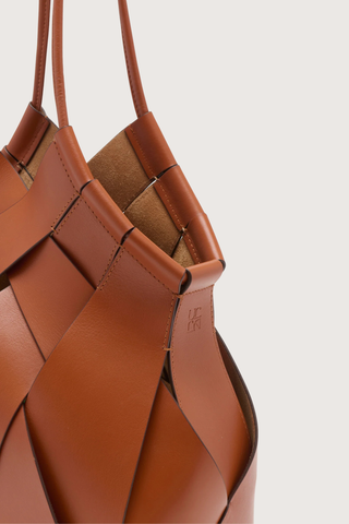close up detail of  Charlotte Shoulder Bag sierra brown basket weaving style
Hand-painted edges
Internal suede-lined
Tubular straps
Smooth calfskin leather
Hammered brass toggle at the top
