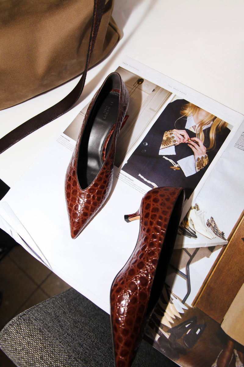croc embossed leather pointy brown heels displayed with a magazine below and white background