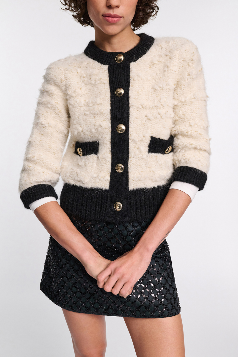 front profile model wearing Delightful Sparkle Cardigan white with black thick trim on collar button closure cuff and pockets. large gold button closure. crewneck. Boxy style has a boucle-like feel and golden D-rose buttons