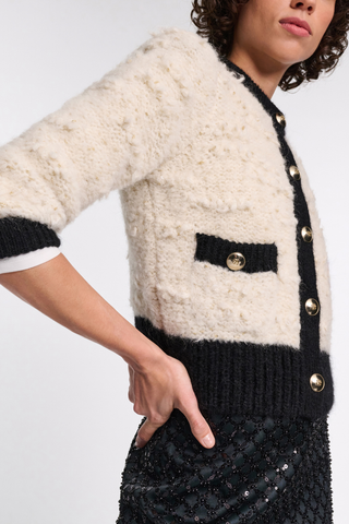 side profile model wearing Delightful Sparkle Cardigan white with black thick trim on collar button closure cuff and pockets. large gold button closure. crewneck. Boxy style has a boucle-like feel and golden D-rose buttons