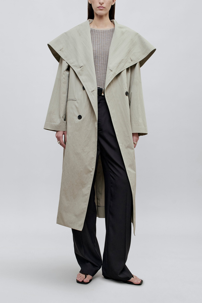 front profile model wearing coat unbuttoned Dorothy Trench Coat fog grey 
Dramatic oversized shawl collar drapes across the shoulders 
Double breasted closure with contrast buttons and self tie belt at the waist
Welt pockets at front
 dropped shoulders and bracelet length sleeves mid calf length cotton nylon blend
