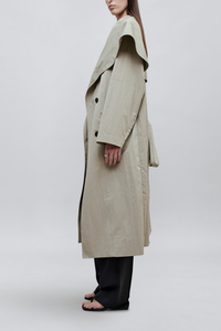 side profile model wearing Dorothy Trench Coat fog grey 
Dramatic oversized shawl collar drapes across the shoulders 
Double breasted closure with contrast buttons and self tie belt at the waist
Welt pockets at front
 dropped shoulders and bracelet length sleeves mid calf length cotton nylon blend