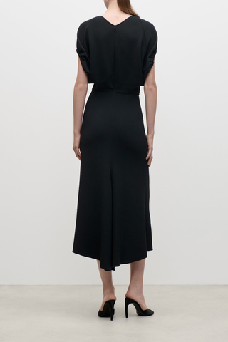 back profile model wearing  Edith Midi Fluid Cady Dress black Gathered sleeve
Directional rope edging
Front v-neckline with tonal topstitching
Flattering fitted waist
Longer-length hemline at the back
Blouson sleeve
Subtle asymmetrical hem
50% Viscose 47% Acetate 3% Elastane