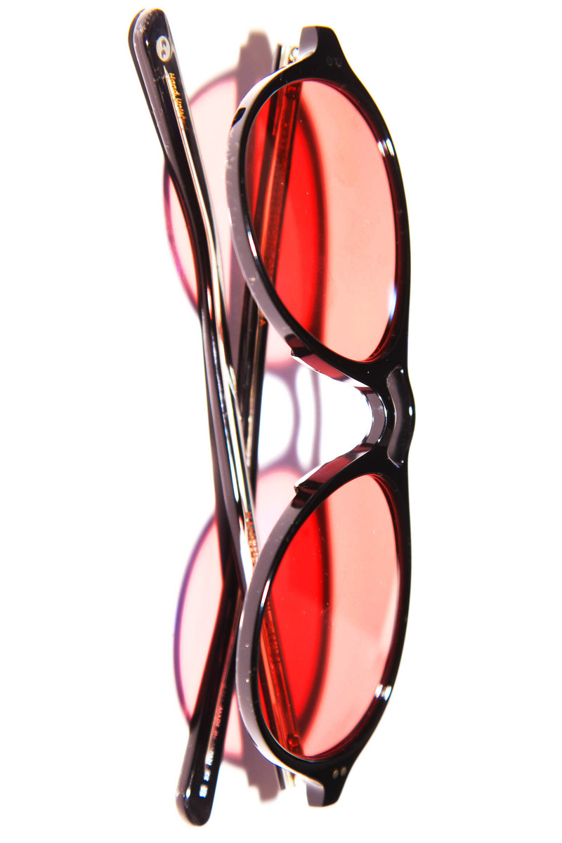 vertical flatlay of pink lens senuglasses with black frame and hard lighting shadow with white solid background