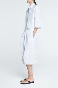 side profile model wearing Lace Tulip Skirt White Tulip shaped 
Elastic waistband
Hidden side pockets
Midi length
Slit at back
White lace hem
 Organic Cotton sateen
