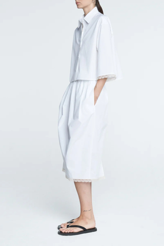 side profile model wearing Lace Tulip Skirt White Tulip shaped 
Elastic waistband
Hidden side pockets
Midi length
Slit at back
White lace hem
 Organic Cotton sateen