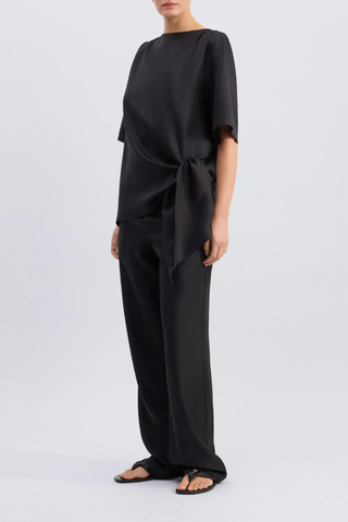 side profile model wearing Mano Short Sleeve Knotted Blouse Black Straight fit
Short sleeves
Boat neck
Gathered fabric at the shoulders
Asymmetric hemline
Knotted waist detail
100% Silk Twill