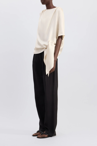 side profile model wearing Mano Short Sleeve Knotted Blouse Ivory Straight fit
Short sleeves
Boat neck
Gathered fabric at the shoulders
Asymmetric hemline
Knotted waist detail
100% Silk Twill