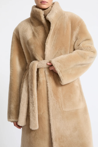 front profile model wearing  tied waist Manteau Reversible Jacket Pampas beige Midi length coat
Two faces of a Merino lambskin shearling
Reversible, it can be worn with the skin side or the wool side facing out
High collar
Matching belt
Welt pockets
Unlined
100% Lamb