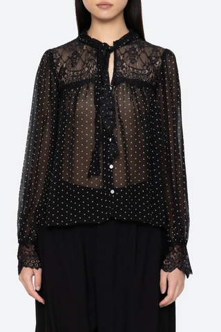front profile model wearing Melody Polka Dot Top black voluminous sleeves softened by delicate lace inserts. Floral buttons and a self-tie closure at the neck