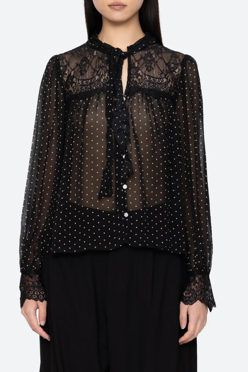 front profile model wearing Melody Polka Dot Top black voluminous sleeves softened by delicate lace inserts. Floral buttons and a self-tie closure at the neck