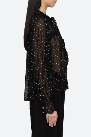 side profile model wearing Melody Polka Dot Top black voluminous sleeves softened by delicate lace inserts. Floral buttons and a self-tie closure at the neck
