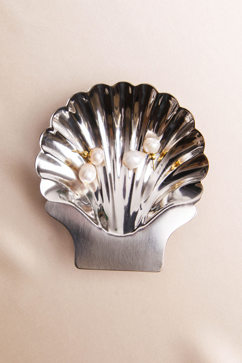 Silver shell tray with pearl earrings and silk beige background