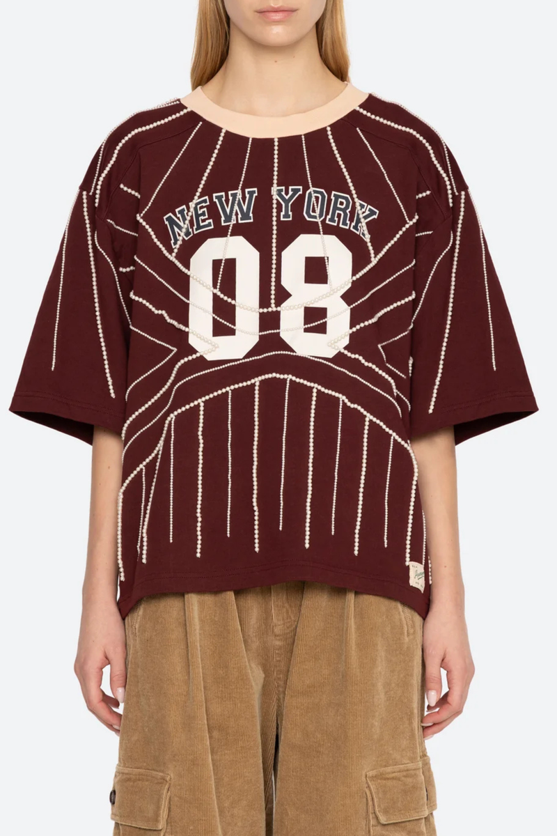 front profile model wearing Quinn T-Shirt burgundy Beaded t-shirt
Inspiration from classic sports jerseys
Varsity-style lettering and numerals
Contrast trim at the collar
Intricate pearl beading throughout
Each piece is hand beaded
Slight variations in bead placement, spacing, and natural drape may occur
100% cotton
Relaxed fit
