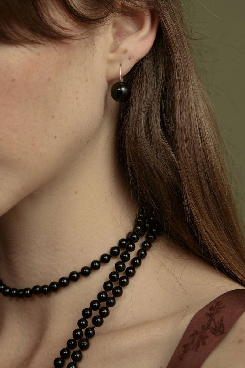 model wearing Rosette Drops Earrings Black Onyx Polished black onyx bead is suspended against a slender sterling silver hoop
Crafted in sterling silver, with round black onyx
Black onyx diameter 12mm