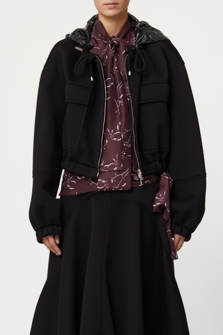 front profile model wearing Scuba Jacket black cropped Scuba viscose, Curled collar with culisse, Front zipped closure, Detachable black shiny hoodie, Two front flap pockets