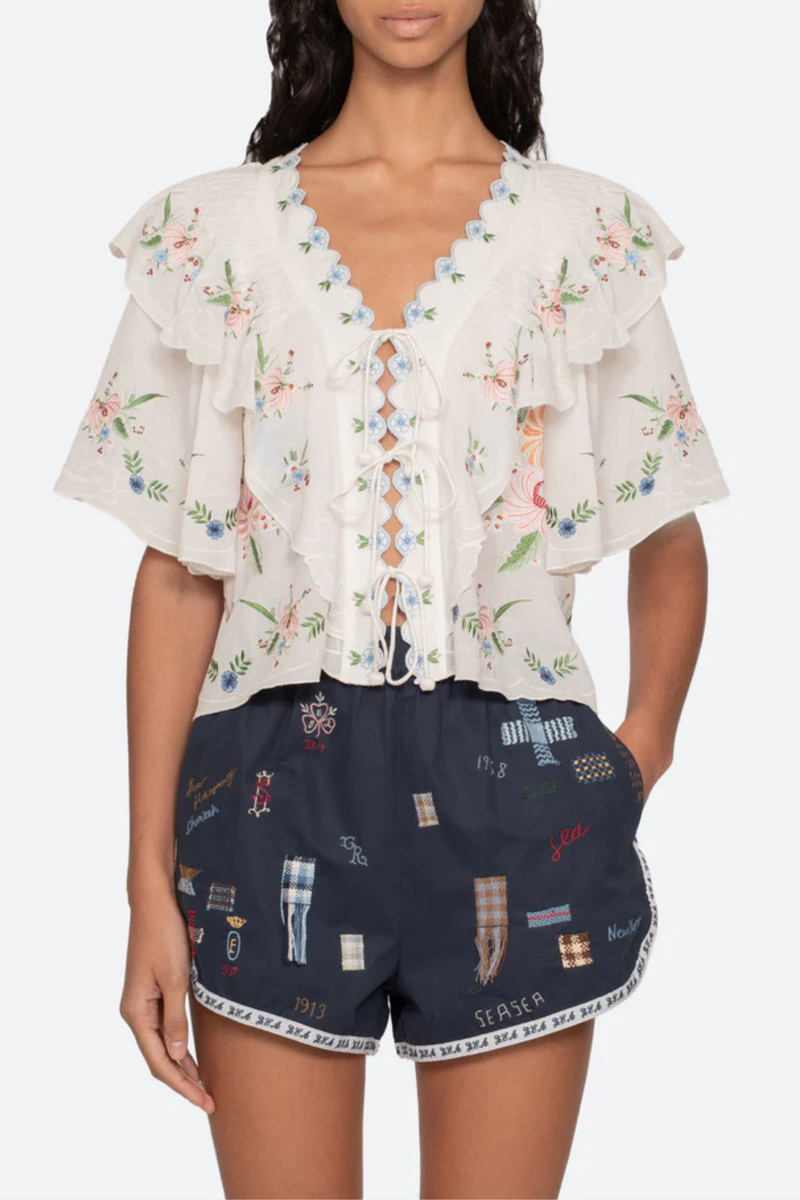 front profile model wearing Serafina Embroidered Front Tie Embroidered short sleeve top
Intricate floral embroidery throughout
Flattering v-neckline
Scalloped edges
Self-tie closures
Tie front closure
