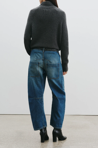 back profile model wearing Shon Jeans Bedford mid blue Wash Mid-rise, relaxed fit barrel leg jean. Uniquely curved silhouette. Seam detail at knees.