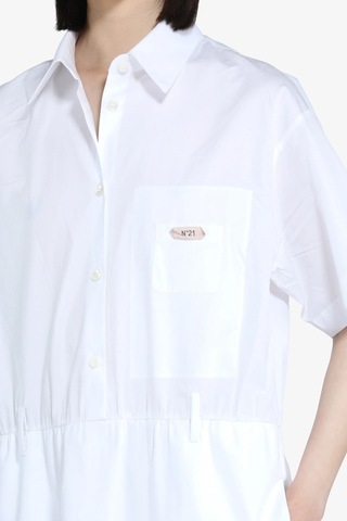 close up detail of Short Sleeve Poplin Dress White  cotton White shirt dress
Classic collar
Short sleeves
Button-up front
Shirtdress style
Elastic waistband
Hem is finished with a ruffle
Above-the-knee length