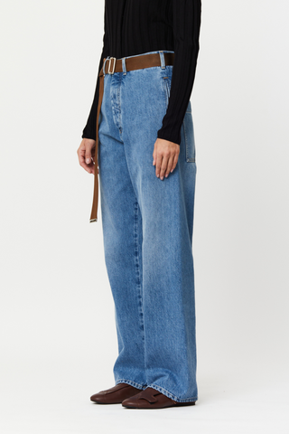 side profile model wearing Straight Leg Belted Jeans, Silver button closure,Two side slant pockets, Two back flat pockets, Embossed Pili and Bianca leather label, Relaxed fit, mid blue wash