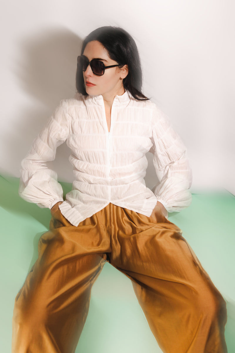 Woman wearing a white blouse and brown pants against a light green background