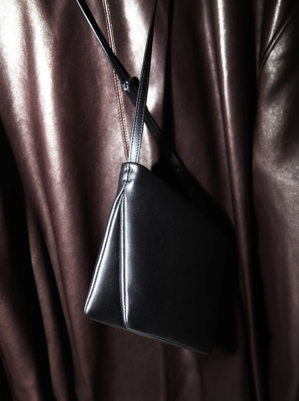 Black crossbody leather bag with brown leather background