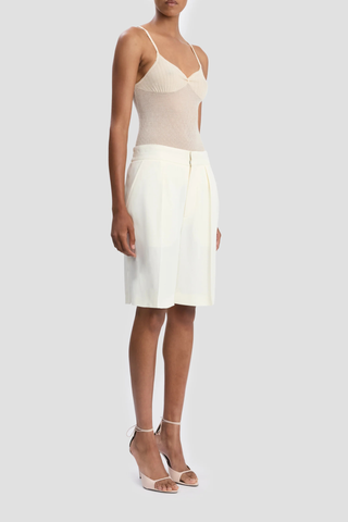 side profile model wearing Tailored Fluid Twill Short ivory Recycled fluid wool fabrication
Knee length
Elasticated back waistband
Zip fly with hook &amp; bar closure
Front pleats
Side pockets
Back jet pockets