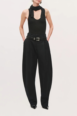 front profile model wearing  The Dean Cotton Pant black High-rise with front pleats
Voluminous tapered leg
Hits at the ankle
Belt loops
Self: 100% Cotton
Lining: 60% Acetate, 40% Polyester