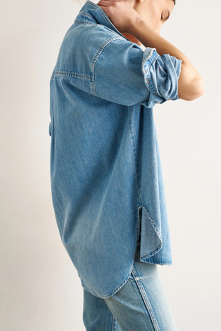 side profile model wearing The Essential Denim Shirt worn indigo mid wash blue relaxed shape
Button at the chest 
Button under the neckline 
Small button perfectly placed on the hidden cuff placket 
100% Cotton
Medium faded vintage inspired indigo 
