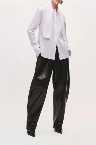 front profile model wearing The Inez Tuxedo Shirt With Tie Neck Scarf white cotton poplin Crisp shirting
Tuxedo-inspired silhouette
Pintucked front detailing
Integrated neck scarf
Pointed collar
Long sleeves
Elongated pintucked cuffs
Button-front closure
Curved shirttail hem