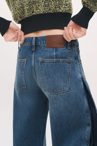 close up back profile of logo leather patch and back pocket for The Lana Trouser Denim bi-color blue mid wash
Wide-leg
Split seam construction
Integrated side pleats 
Classic five-pocket construction
Back darts in place of a traditional denim yoke
Brown denim back patch
Zip fly with button closure
100% Cotton
