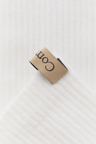close up ribbon detail for The Merino Tube Sock Off White 
68% Merino Wool, 30% Nylon, 2% Elastane
Terry cushioned footbed
With logo ribbon tab