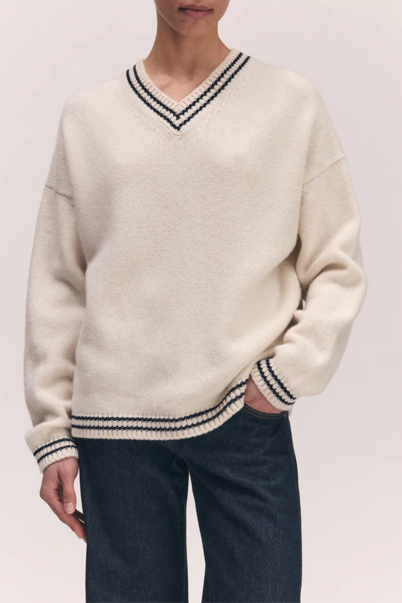 front profile model wearing The Stripe Trim Balla V-Neck Sweater lambswool white with navy stripe detail on neck, hem and cuff 