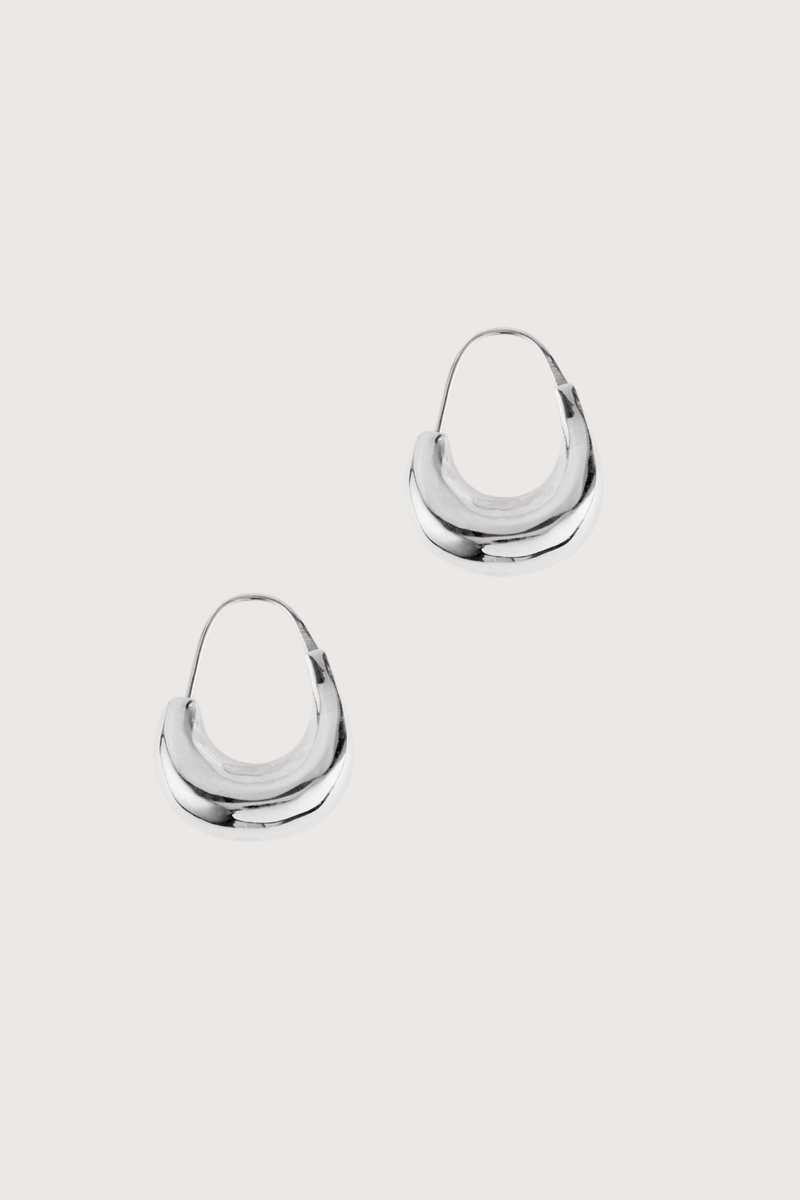 flat lay Tide Hoops Silver Small irregular loop
Weighted and organic form that curls just below the lobe
Sterling silver and plated in rhodium
Earring length approximately 2.8cm