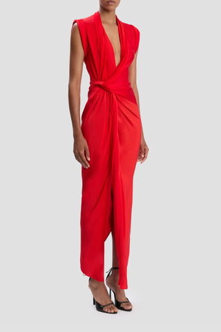 side profile model wearing Twist Detail CDC Dress Red Asymmetric, drape midi dress
High shine jersey bodice
Crepe de chine skirt
Wrap front neckline with button &amp; thread loop closure
Short roll sleeve
Twist drape waist detail
Front skirt split
Concealed side zip