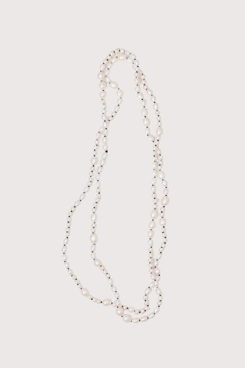 flat lay Veil Pearl Necklace Irregular shaped pearls
Threaded and knotted onto a contrasting black silk
Can be worn doubled around the neck, crossed over the body as a sash from the sea, or crafted into a belt to provide luster and accent to layered fabric
Baroque pearls and black silk
Necklace measures 1.2 meters in length
