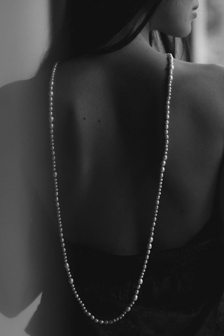 model wearing Veil Pearl Necklace Irregular shaped pearls
Threaded and knotted onto a contrasting black silk
Can be worn doubled around the neck, crossed over the body as a sash from the sea, or crafted into a belt to provide luster and accent to layered fabric
Baroque pearls and black silk
Necklace measures 1.2 meters in length