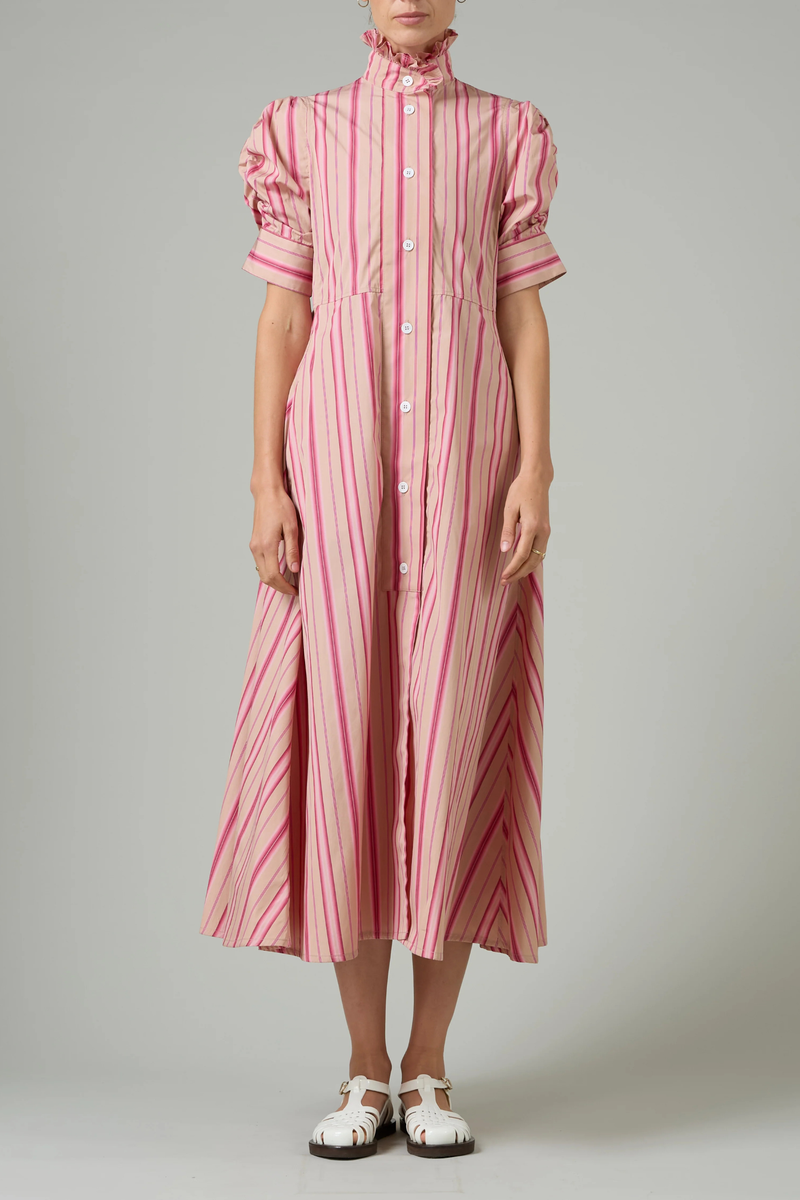 front profile model wearing Venetia Stripe Short Sleeve Dress  biscuit pink stripe High neck with ruffle trim
Button front closure
Puff sleeves
Ruched sleeve with thick cuffs
Midi length
Vertical stripes
100% Cotton