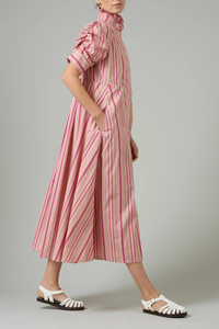 side profile model wearing Venetia Stripe Short Sleeve Dress  biscuit pink stripe High neck with ruffle trim
Button front closure
Puff sleeves
Ruched sleeve with thick cuffs
Midi length
Vertical stripes
100% Cotton