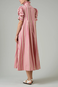 back profile model wearing Venetia Stripe Short Sleeve Dress  biscuit pink stripe High neck with ruffle trim
Button front closure
Puff sleeves
Ruched sleeve with thick cuffs
Midi length
Vertical stripes
100% Cotton