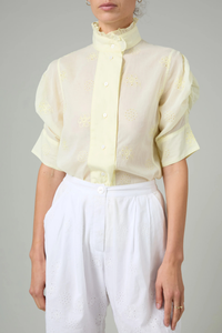 front profile model wearing Vita Embroidered Voile Short Sleeve Top yellow Embroidery throughout
Puff sleeves
Ruched sleeves with thick cuffs
High collar with ruffles
Button front

Side slit
100% Cotton