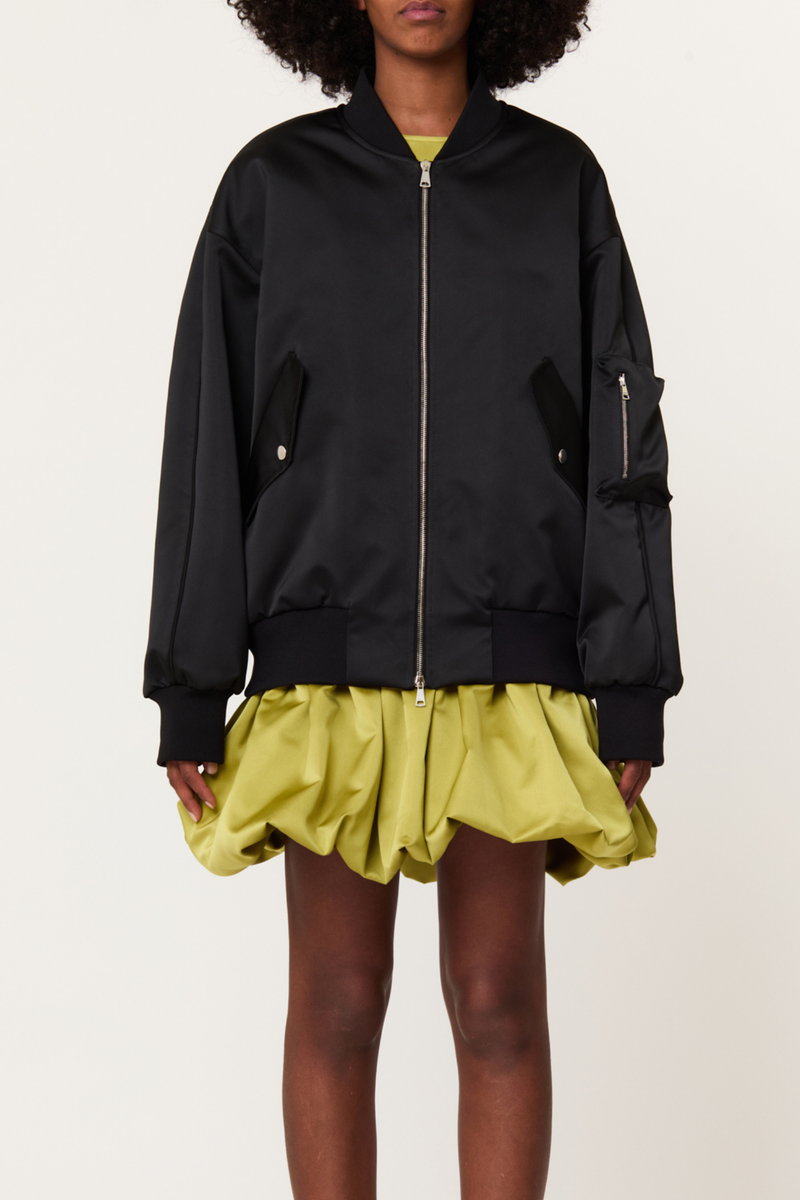 front profile model wearing  Zip Front Long Baseball Jacket black Bomber jacket
Refined duchesse
Slightly oversized fit
High elasticated waistband
Wide sleeves
Dropped shoulders for a relaxed look
Ribbed bomber collar
Central double-slider metal zip
Side flap pockets with snap buttons
Signature MA-1 zipped utility pocket on the left sleeve
71% Polyester 29% Nylon lining 71% Cupro