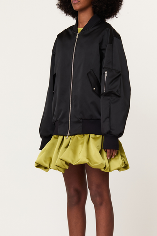 side profile model wearing  Zip Front Long Baseball Jacket black Bomber jacket
Refined duchesse
Slightly oversized fit
High elasticated waistband
Wide sleeves
Dropped shoulders for a relaxed look
Ribbed bomber collar
Central double-slider metal zip
Side flap pockets with snap buttons
Signature MA-1 zipped utility pocket on the left sleeve
71% Polyester 29% Nylon lining 71% Cupro