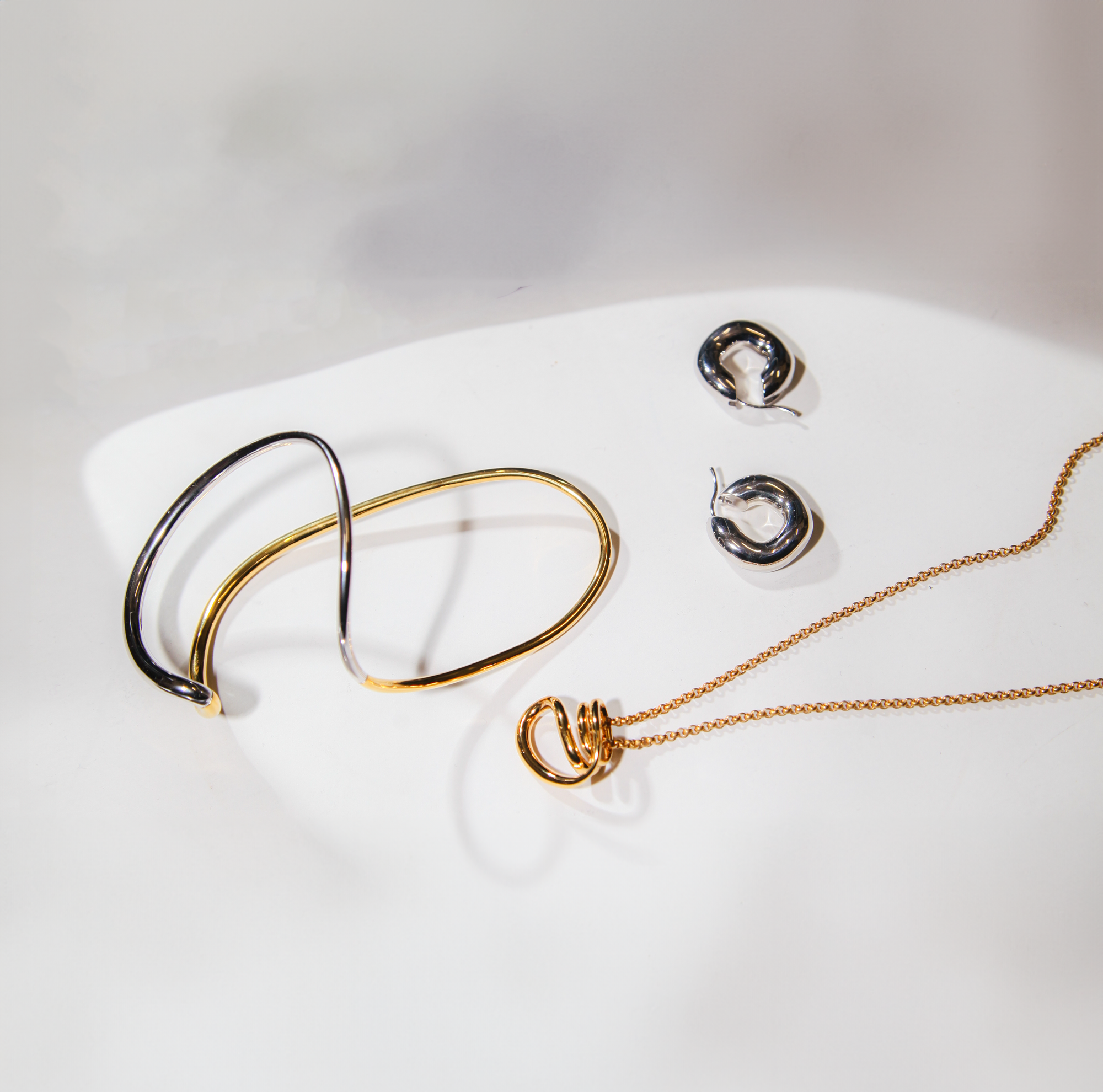 white background showcasing sterling silver and gold vermeil mixture cuff bracelet, sterling silver hoop earrings, and gold vermeil necklace from designer charlotte chesnais. 