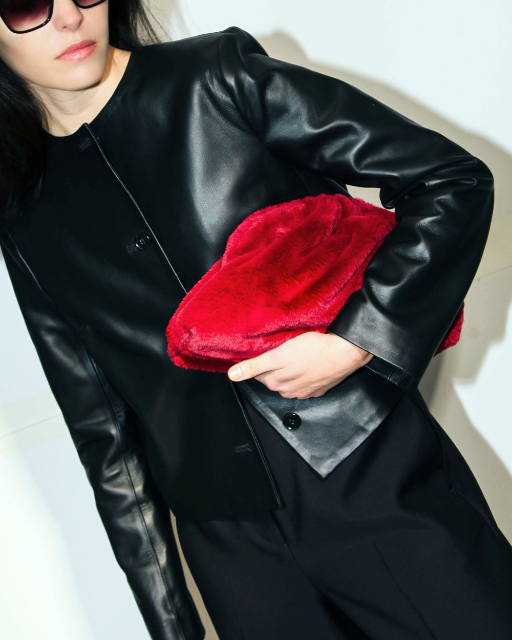 person wearing black leather jacket, red clutch, and black pants